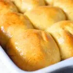 Freshly baked honey butter rolls on a wooden table with honey drizzle.